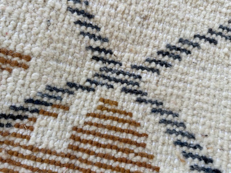 May include: Close-up of a woven rug with a geometric pattern in shades of brown, white, and gray.