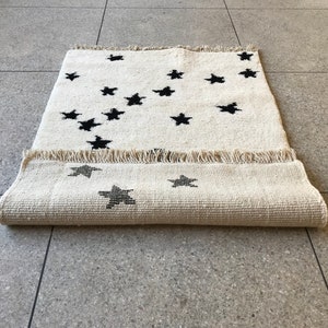 May include: A white rug with a black star pattern. The rug is rolled up and has a fringe border.