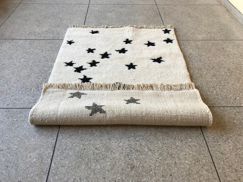 May include: A white rug with a black star pattern. The rug is rolled up and has a fringe border.