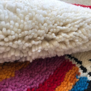 May include: Close-up of a white, fluffy rug with a colorful striped pattern underneath. The rug is made of wool and has a soft, textured surface.