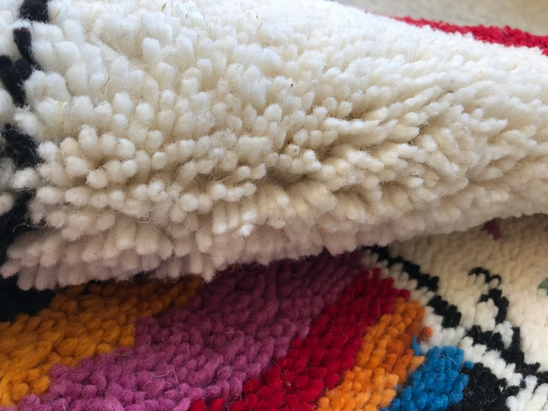 May include: Close-up of a white, fluffy rug with a colorful striped pattern underneath. The rug is made of wool and has a soft, textured surface.