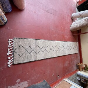May include: A white and black patterned rug with fringe on the ends. The rug is laid out on a red tiled floor.