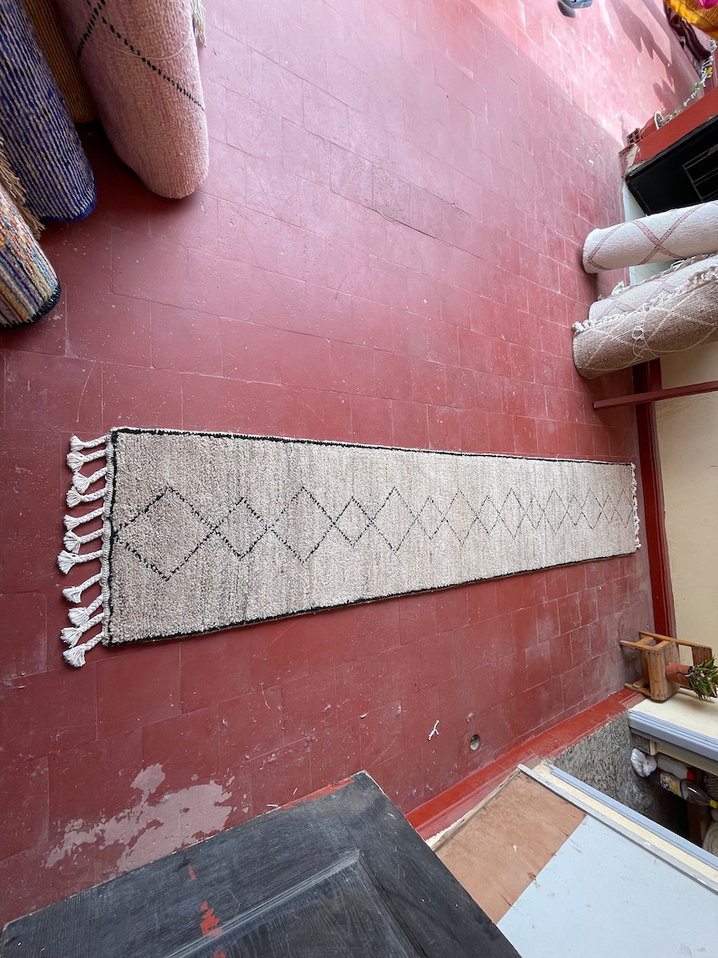 May include: A white and black patterned rug with fringe on the ends. The rug is laid out on a red tiled floor.