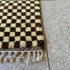 May include: A brown and white checkered rug with fringe. The rug is made of a soft, fluffy material.