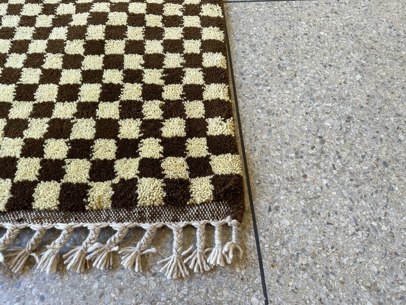 May include: A brown and white checkered rug with fringe. The rug is made of a soft, fluffy material.