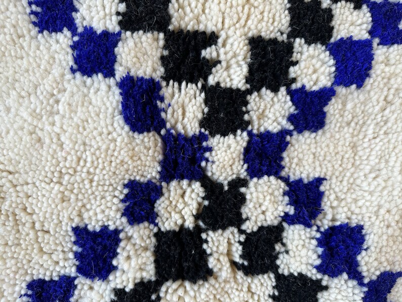 May include: Close-up of a white, black, and blue Moroccan rug with a checkered pattern. The rug is made of wool and has a soft, fluffy texture.
