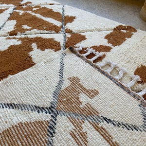 May include: A close-up of a white and brown patterned rug with a fringe border. The rug has a geometric design with brown and white stripes.