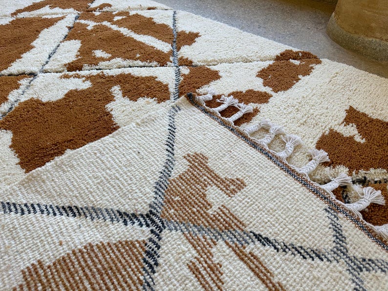 May include: A close-up of a white and brown patterned rug with a fringe border. The rug has a geometric design with brown and white stripes.