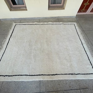 May include: A white shag rug with a black border. The rug has a fringe around the edges.