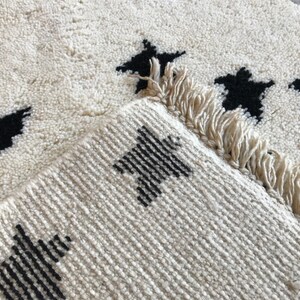 May include: A white rug with black star designs. The rug has a fringe border.
