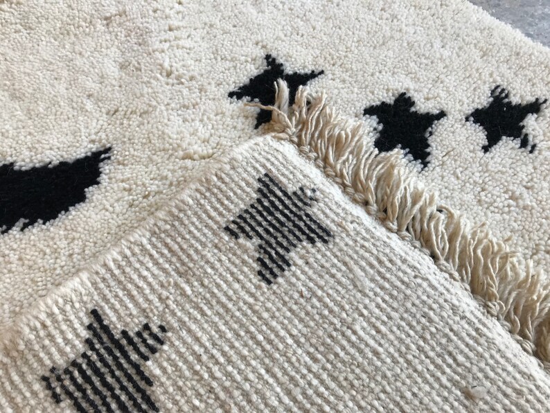 May include: A white rug with black star designs. The rug has a fringe border.