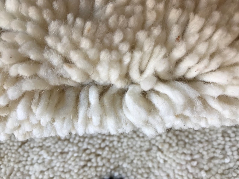 May include: Close-up of a white, fluffy rug with a long, shaggy pile. The rug has a two-toned texture, with a denser, shorter pile in the lower portion.