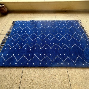 Puede incluir: Una alfombra azul y blanca con un borde de flecos. La alfombra tiene un dise&ntilde;o geom&eacute;trico con diamantes blancos y zigzags sobre un fondo azul.