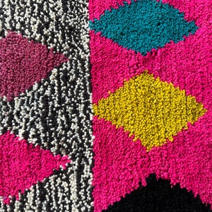 K&ouml;nnte beinhalten: Nahaufnahme eines bunten Teppichs mit geometrischem Muster. Der Teppich besteht aus einem weichen, flauschigen Material und weist Farbt&ouml;ne von Rosa, Gelb, Blau, Schwarz und Wei&szlig; auf.