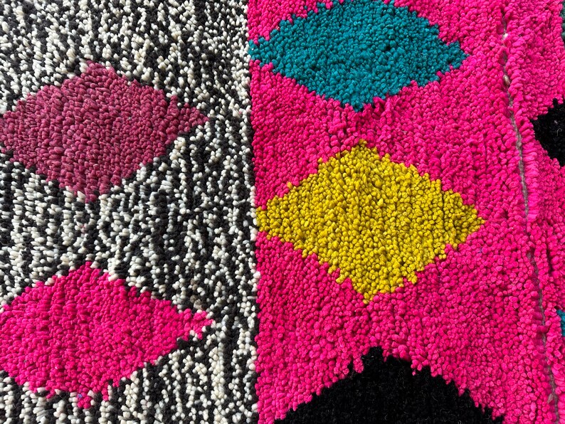 K&ouml;nnte beinhalten: Nahaufnahme eines bunten Teppichs mit geometrischem Muster. Der Teppich besteht aus einem weichen, flauschigen Material und weist Farbt&ouml;ne von Rosa, Gelb, Blau, Schwarz und Wei&szlig; auf.