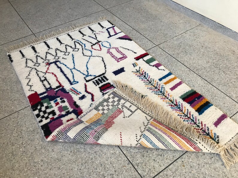 May include: A white rug with a colorful geometric pattern. The rug has a fringe border and is made of wool.