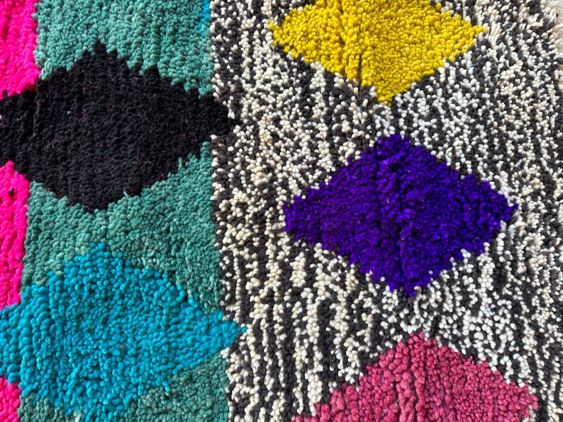 K&ouml;nnte beinhalten: Ein bunter marokkanischer Teppich mit geometrischen Mustern in den Farben Rosa, Blau, Gr&uuml;n, Gelb, Lila, Schwarz und Wei&szlig;.