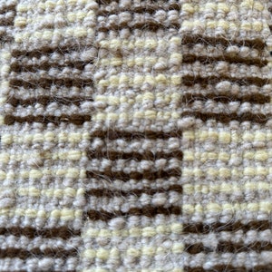 May include: Close-up of a woven fabric with a checkered pattern in shades of brown and cream.