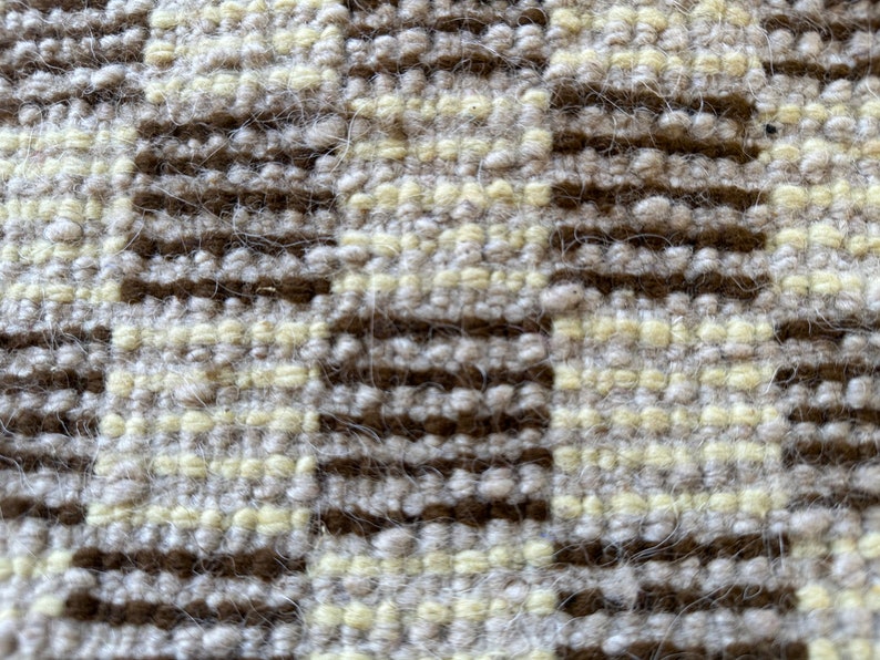 May include: Close-up of a woven fabric with a checkered pattern in shades of brown and cream.