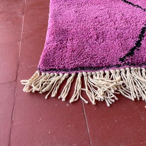 May include: A pink and black rug with a fringe border. The rug has a geometric pattern and is made of a soft, fluffy material.