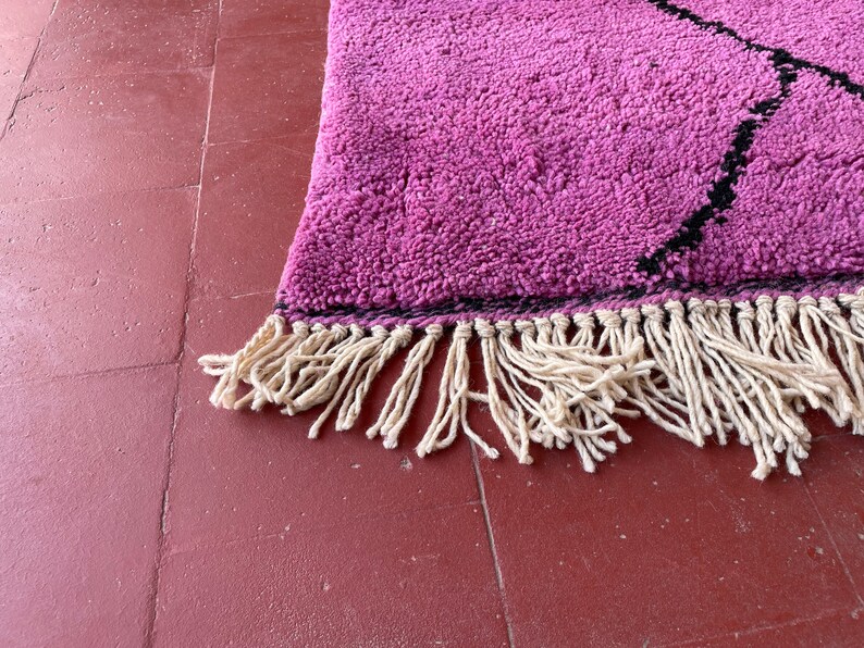 May include: A pink and black rug with a fringe border. The rug has a geometric pattern and is made of a soft, fluffy material.