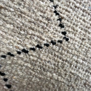 May include: Close-up of a beige rug with a black geometric pattern. The rug has a textured, woven look.