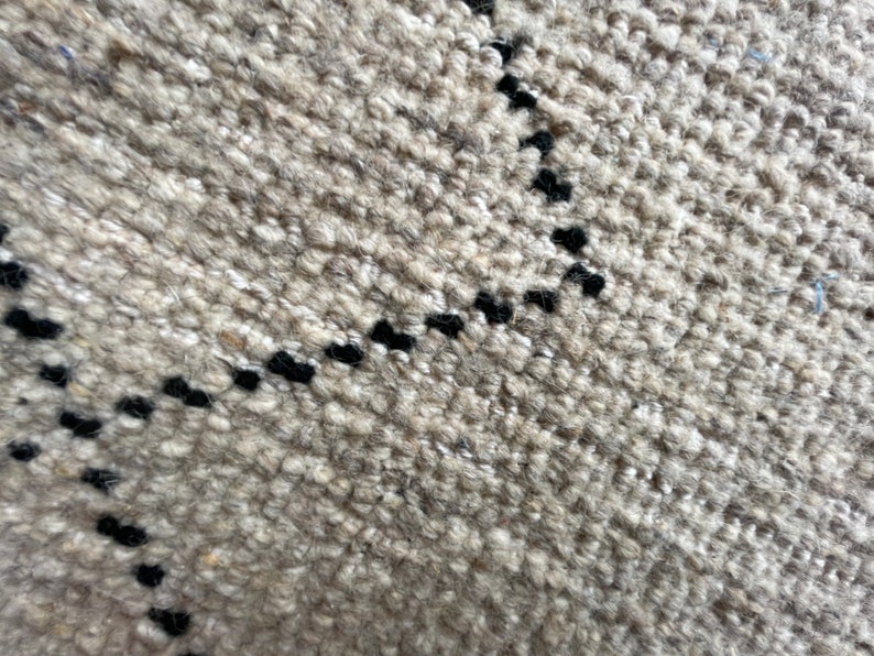 May include: Close-up of a beige rug with a black geometric pattern. The rug has a textured, woven look.