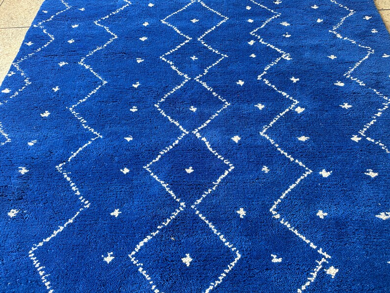 Puede incluir: Una alfombra azul con un patr&oacute;n de diamantes blancos. La alfombra tiene una textura suave y esponjosa.
