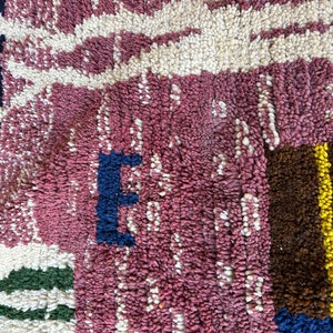 Puede incluir: Primer plano de una alfombra tejida de color rosa, blanco, azul, verde, marr&oacute;n y amarillo con un patr&oacute;n geom&eacute;trico. La alfombra est&aacute; hecha de hilo grueso y texturizado.