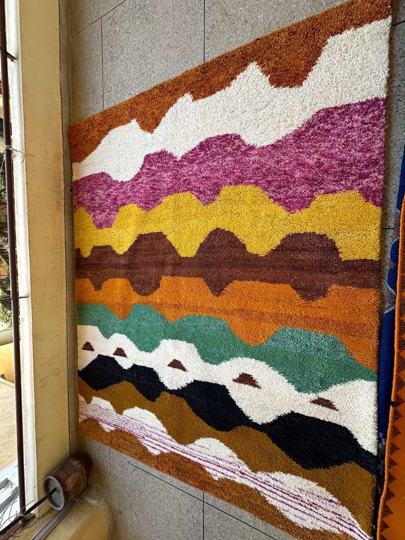 May include: A colorful rug with a wavy pattern in shades of brown, orange, yellow, pink, white, green, and black.