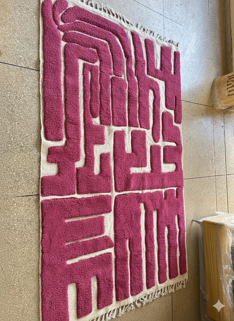 May include: A rectangular rug with a geometric design in shades of fuchsia and white. The rug features a textured, raised pattern in fuchsia against a white background. The edges are finished with a fringe.