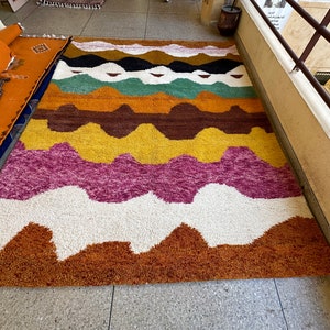 May include: A colorful, abstract rug with wavy lines in shades of brown, yellow, pink, green, and white. The rug has a fluffy texture and is perfect for adding a touch of bohemian style to any room.