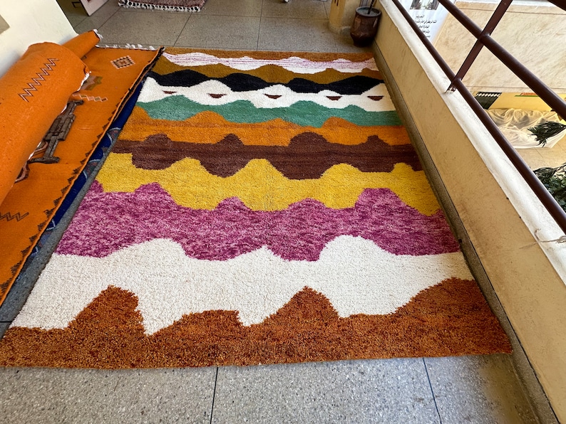 May include: A colorful, abstract rug with wavy lines in shades of brown, yellow, pink, green, and white. The rug has a fluffy texture and is perfect for adding a touch of bohemian style to any room.