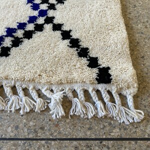 May include: A white rug with black and blue geometric patterns and white fringe.