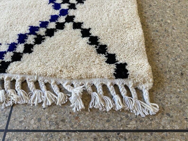 May include: A white rug with black and blue geometric patterns and white fringe.