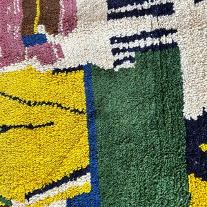 Puede incluir: Primer plano de una alfombra colorida con patrones geom&eacute;tricos en tonos de rosa, amarillo, verde, azul, blanco y marr&oacute;n. La alfombra est&aacute; hecha de un material suave y texturizado.