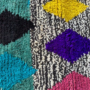 K&ouml;nnte beinhalten: Ein bunter marokkanischer Teppich mit geometrischen Mustern in den Farben Rosa, Blau, Gr&uuml;n, Gelb, Lila, Schwarz und Wei&szlig;.