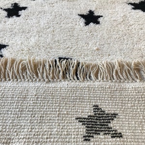 May include: A white rug with black star designs and fringe edging. The rug is made of a soft, woven material.