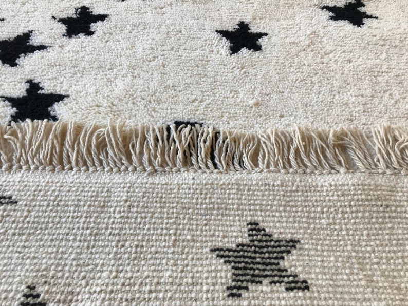 May include: A white rug with black star designs and fringe edging. The rug is made of a soft, woven material.