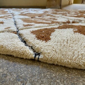 May include: Close-up of a white and brown patterned rug with a black and white border. The rug is made of a soft, fluffy material.