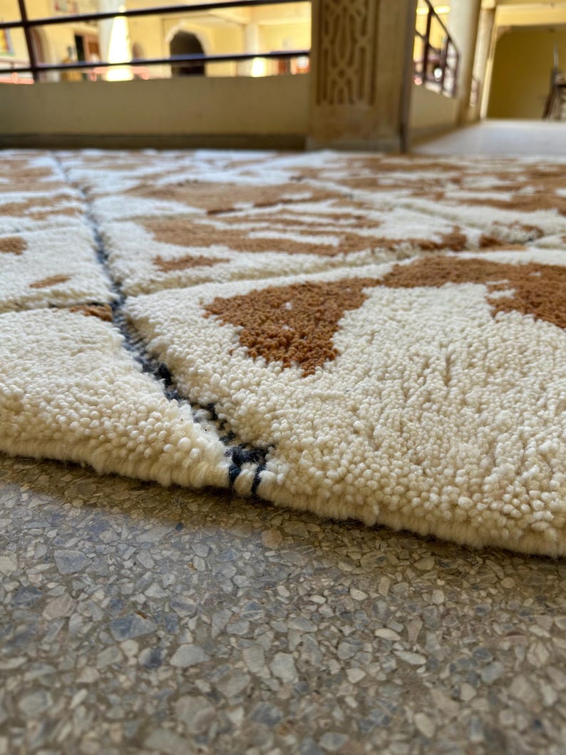 May include: Close-up of a white and brown patterned rug with a black and white border. The rug is made of a soft, fluffy material.