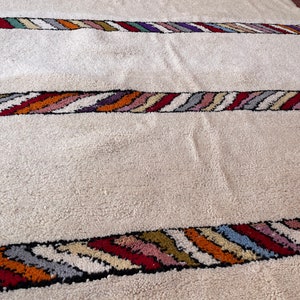 Puede incluir: Una alfombra blanca con rayas onduladas de colores a lo largo de los bordes. Las rayas est&aacute;n hechas de diferentes colores, incluyendo rojo, naranja, amarillo, verde, azul y morado.