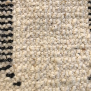 May include: Close-up of a white and black woven rug with a textured surface. The rug has a simple geometric pattern.