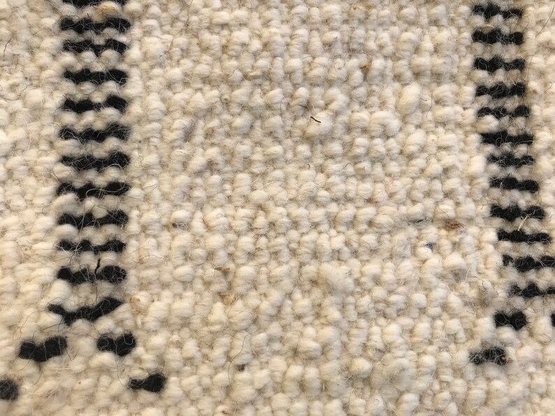 May include: Close-up of a white and black woven rug with a textured surface. The rug has a simple geometric pattern.