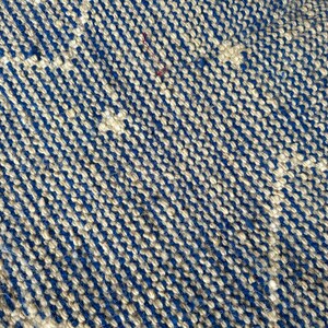 Puede incluir: Primer plano de una alfombra tejida con un patr&oacute;n azul y beige. La alfombra est&aacute; hecha de fibras naturales y tiene una superficie texturizada.
