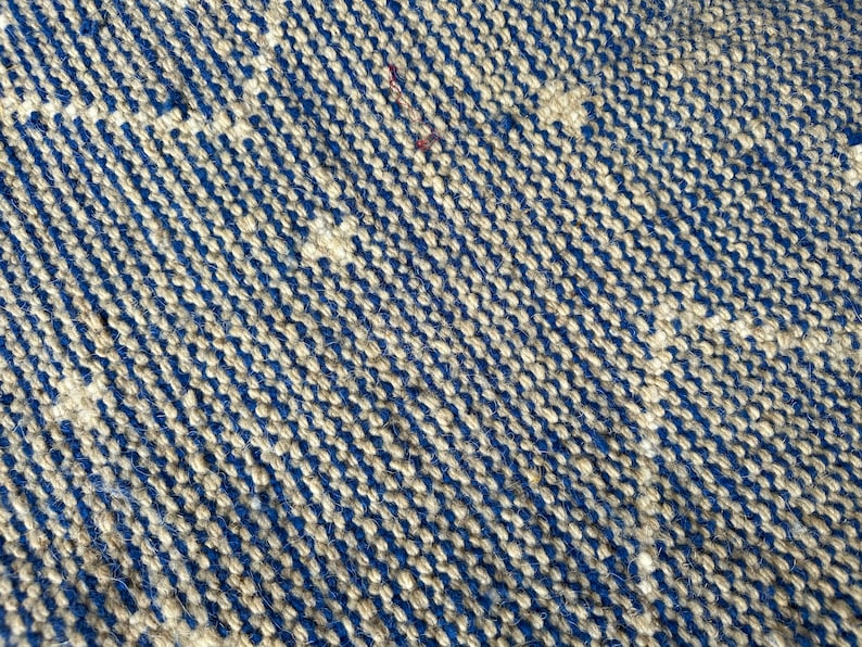 Puede incluir: Primer plano de una alfombra tejida con un patr&oacute;n azul y beige. La alfombra est&aacute; hecha de fibras naturales y tiene una superficie texturizada.