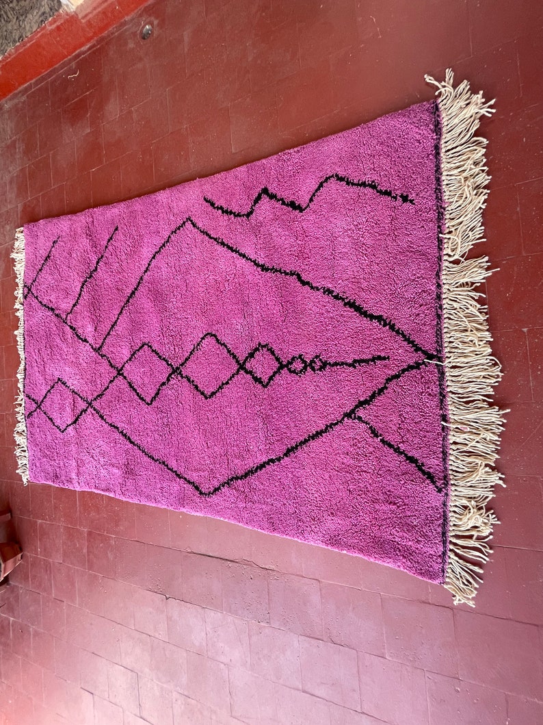May include: A pink and black Moroccan rug with a geometric pattern. The rug has a fringe border.