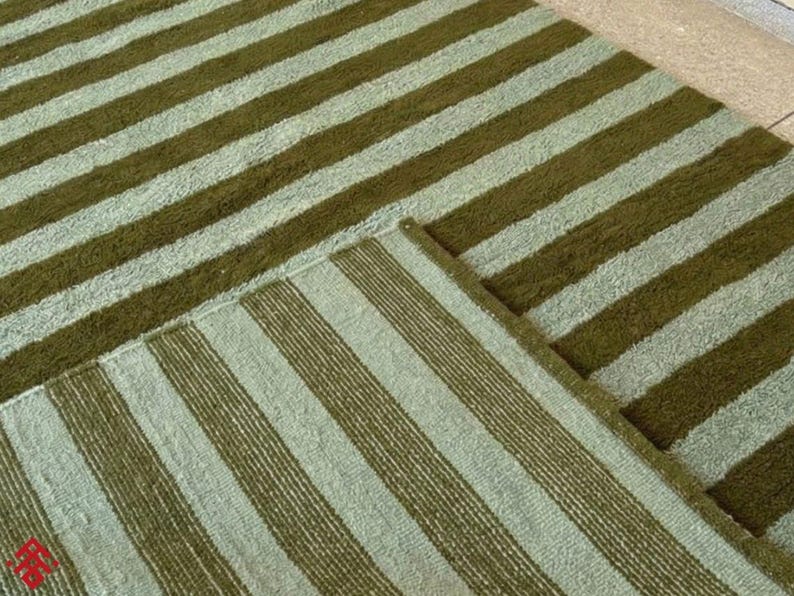 May include: Two rectangular rugs with a striped pattern. The stripes alternate between a light green and a darker olive green. The rugs are made of a textured material and are placed on a light-colored surface.