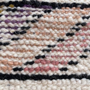 Puede incluir: Primer plano de una alfombra tejida con un patr&oacute;n geom&eacute;trico en tonos de rosa, blanco, negro y morado.