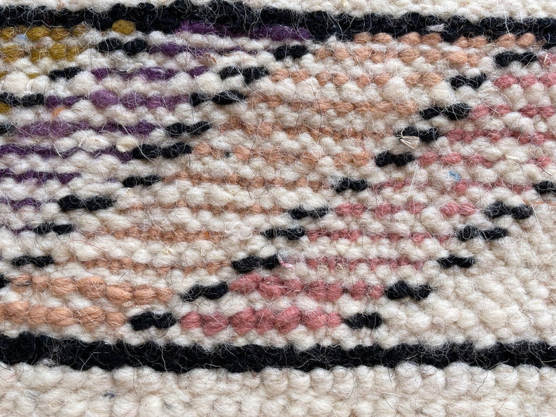 Puede incluir: Primer plano de una alfombra tejida con un patr&oacute;n geom&eacute;trico en tonos de rosa, blanco, negro y morado.